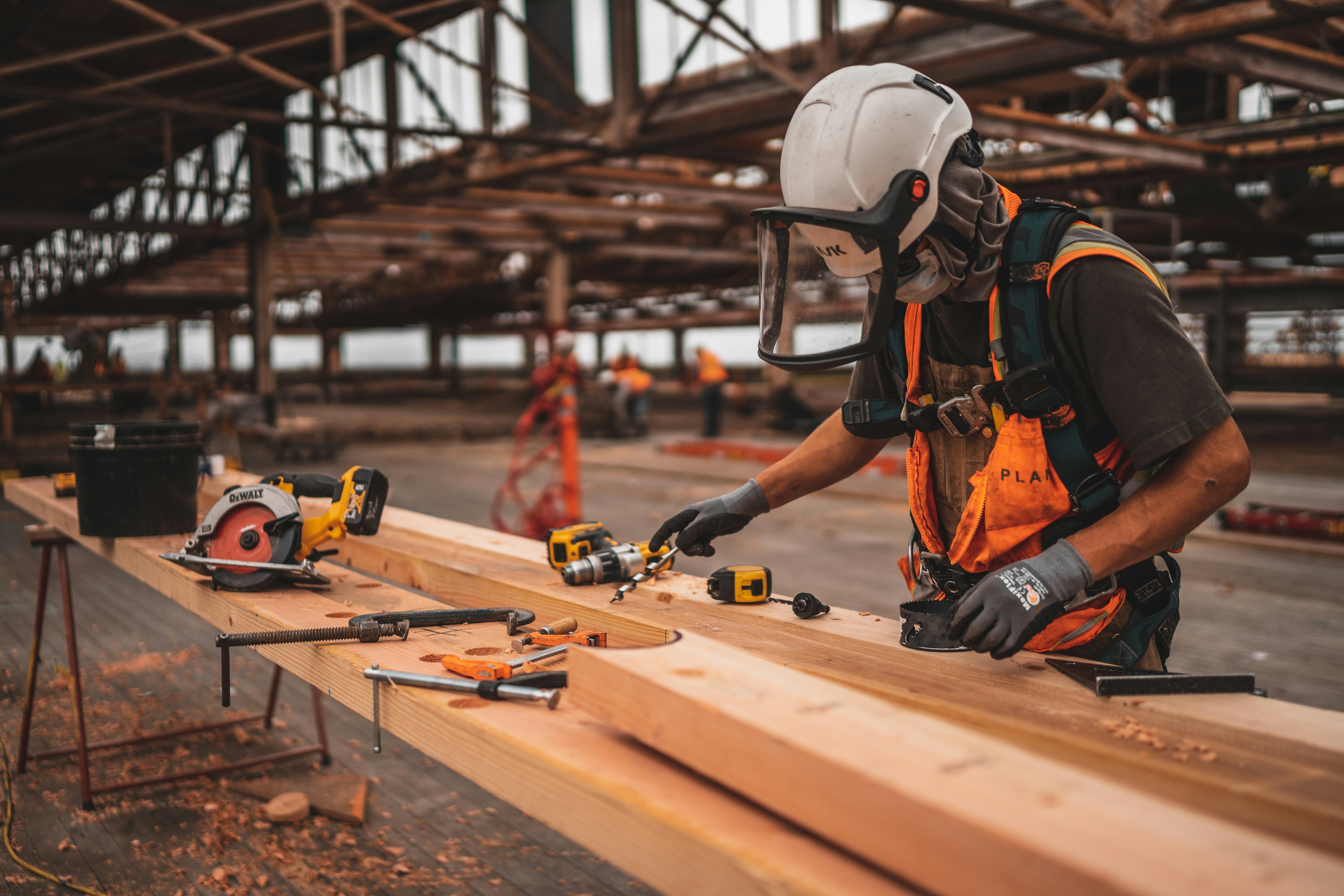 man in orange and black vest wearing white helmet holding yellow and black power toolby Jeriden Villegas